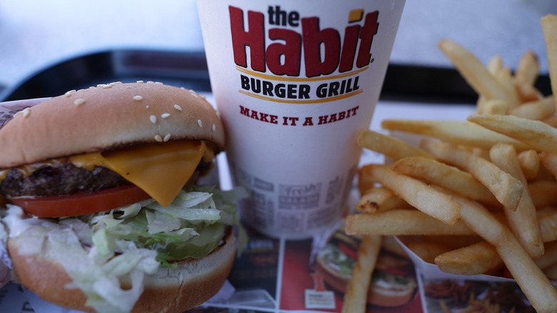 the habit burger with cheese and toppings next to a drink and order of fries