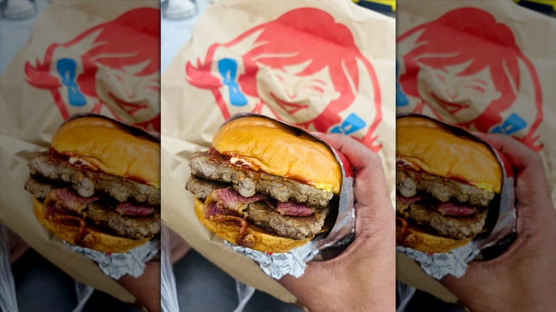 Hand holding a double Wendy's burger in front of packaging with logo