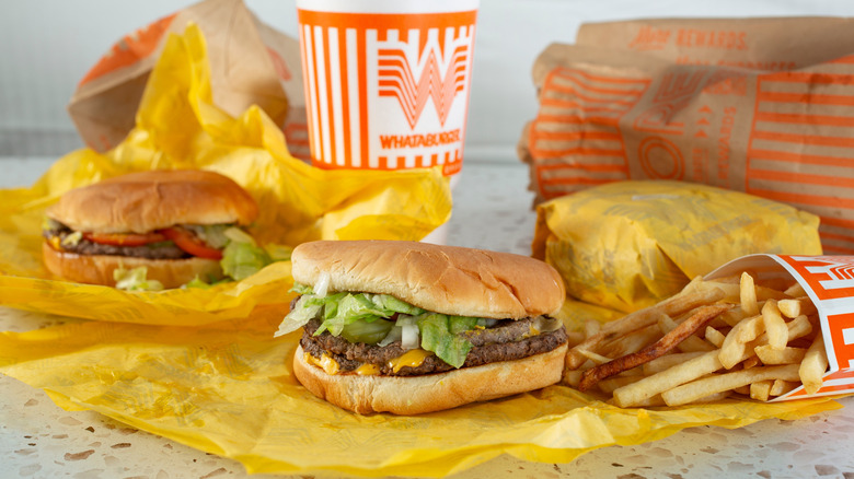 two whataburger burgers on yellow paper next to an order of fries, a large drink, and another burger completely wrapped in paper
