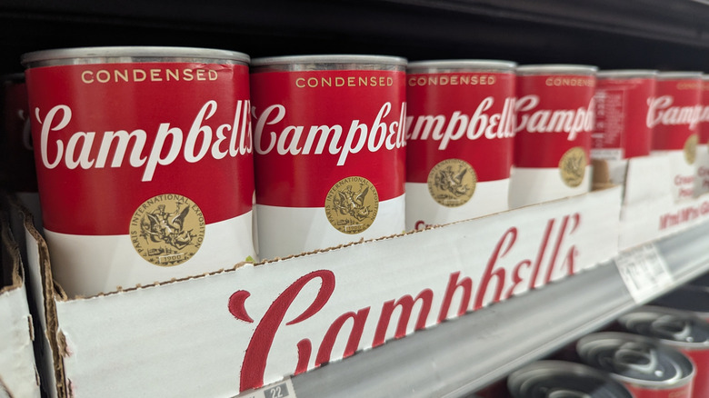Row of Campbell's cans in branded cardboard tray on store shelf