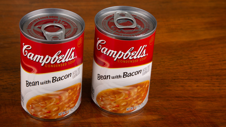 Two Campbell's bean with bacon soup cans on wooden table