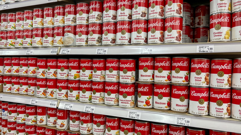 Several rows of different flavors of Campbell's soups in grocery store aisle.