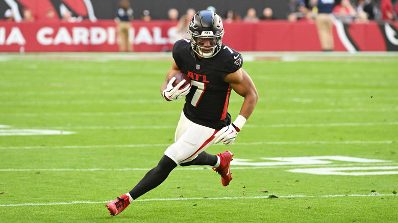 Bijan Robinson running with a football tucked in his right arm while wearing a black Atlanta Falcons jersey