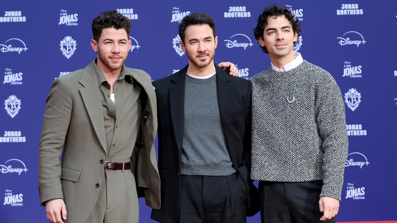 The Jonas Brothers posing in front of a blue and white photo wall at a Disney premier