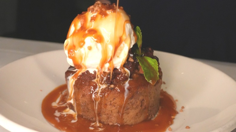 A brown cake covered in ice cream and brown syrup.