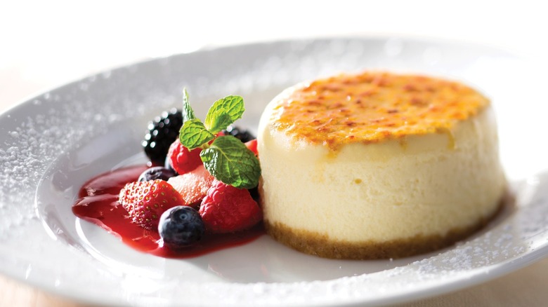 A small cheesecake on a white plate with berries.
