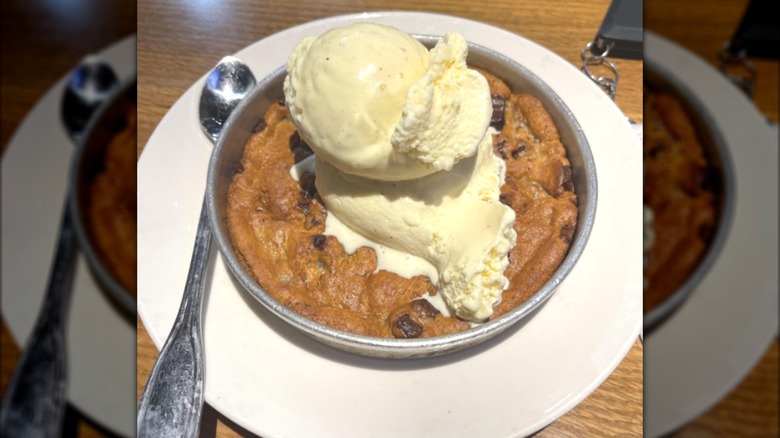 A chocolate chip cookie topped with ice cream in a silver pan.