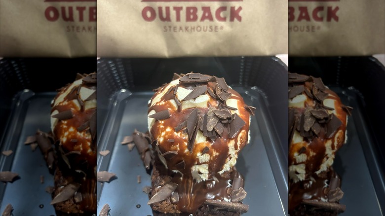 An ice cream and chocolate-covered brownie in a takeout container next to an Outback Steakhouse.