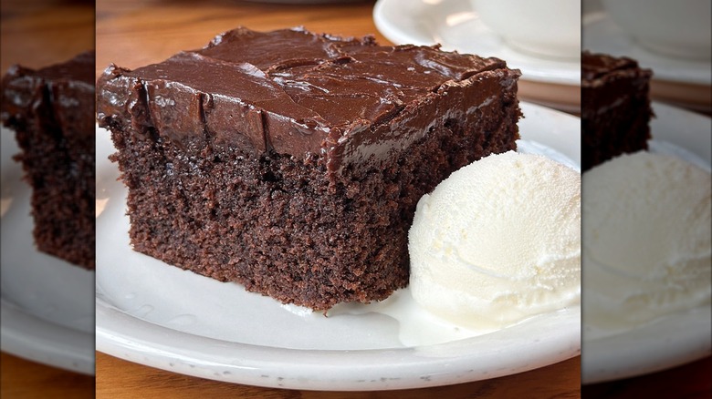 A large slice of chocolate cake and a scoop of ice cream on a white plate.