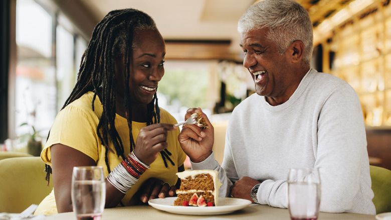 A smiling man and woman eating cake inside a restaurant.