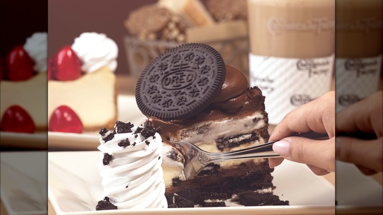 Someone pushing their fork into a slice of Oreo cheesecake.