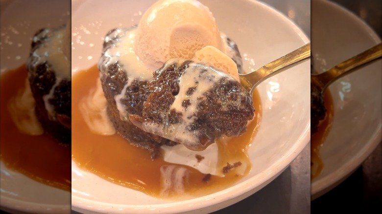 A bowl of sticky toffee pudding with a spoon.