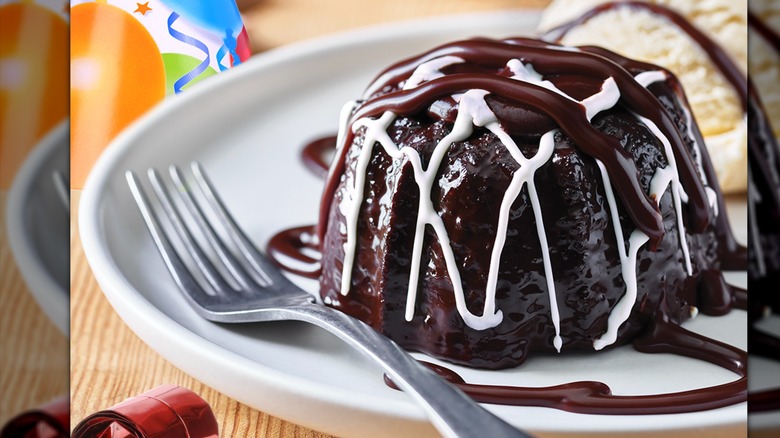 A chocolate cake covered in white and dark sauce on a white plate.