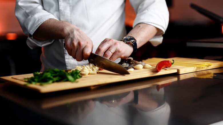 chef cutting vegetables and aromatics with heel of knife on cutting board