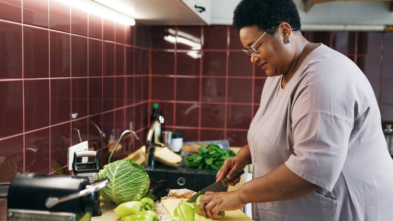 woman chopping vegetables in kitchen with red tiles and fluorescent lights