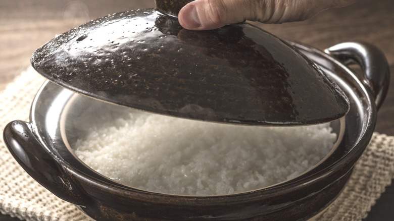 person lifting lid off of black ceramic pot of rice