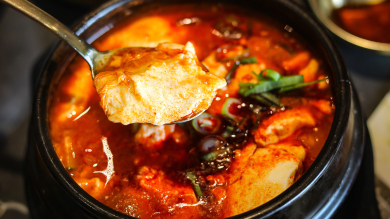 hearty soup in black ceramic dish with close up of spoon taking some soup
