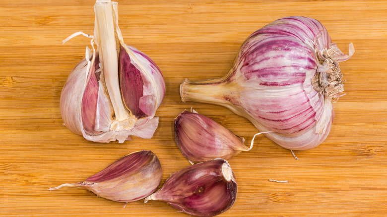 Two heads of garlic on wooden surface next to unpeeled cloves