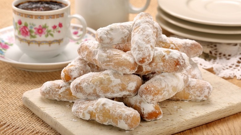 a stack of cylindrical andalusian alfajores covered in powdered sugar sits next to a cup of tea and cutlery