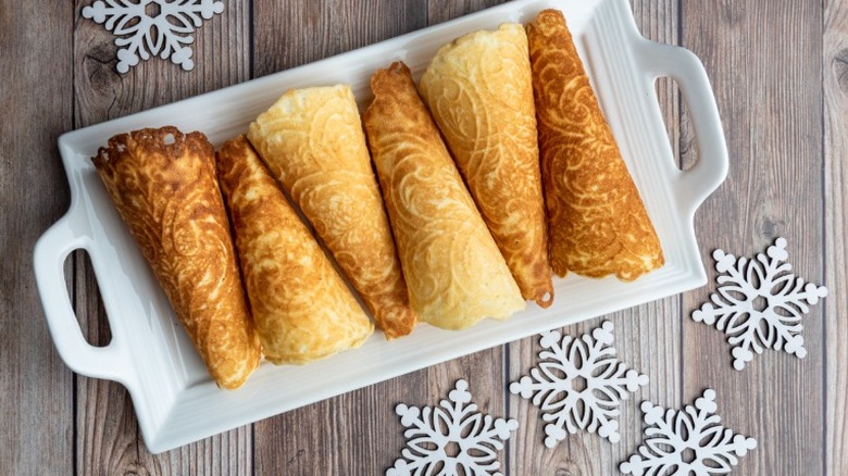 a white plate holding a row of norwegian krumkaker, cone shaped, waffle-like cookies