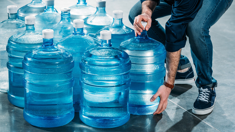A delivery worker picking up a large bottle of water from a group of similar bottles