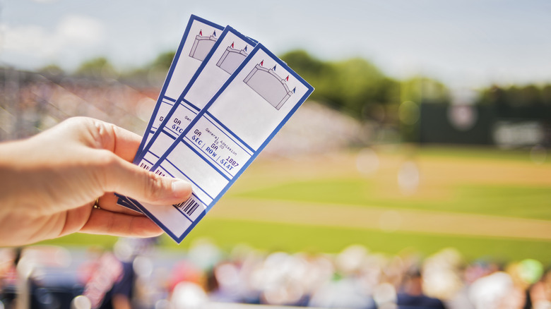 A hand holding sporting tickets in front of a baseball field
