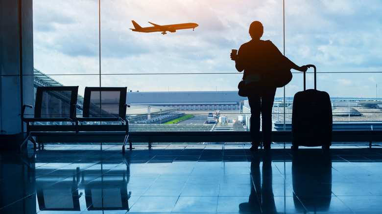 A female traveler looking out of an airport window at a landing airplane