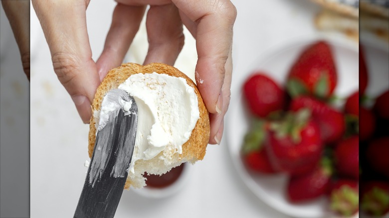 Strawberries in background with hand spreading cream cheese on biscuit bread