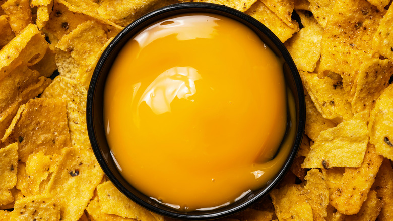 Closeup view of nachos tortilla chips with cheese sauce in a black bowl.