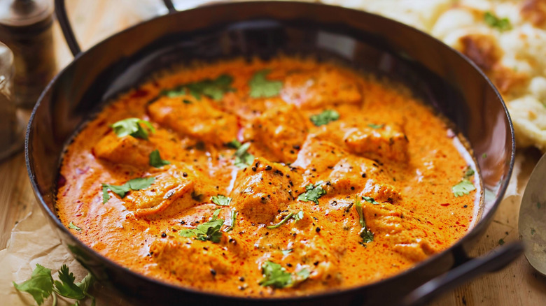 A vibrant bowl of chicken curry, showcasing tender chicken pieces simmered in a rich, aromatic sauce, infused with spices and garnished with fresh cilantro. The golden hue and inviting aroma promise a