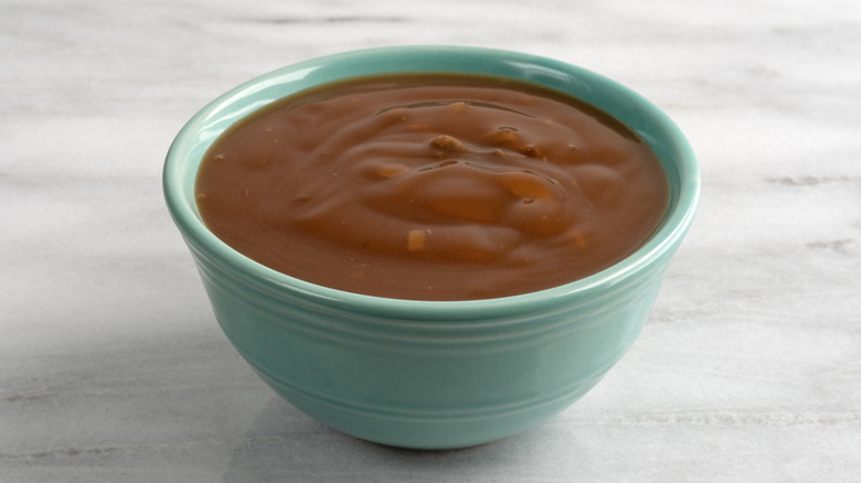 A bowl of mushroom gravy with small chunks of beef on a gray marble table.