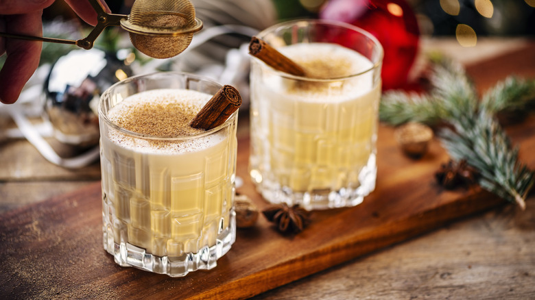 eggnog with cinnamon sticks in glasses on wooden surface