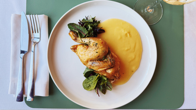 Chicken thigh on white plate with fork and knife