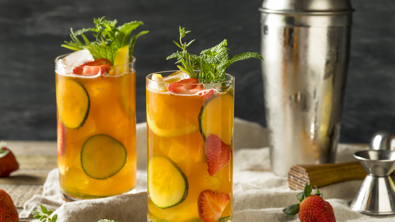Two Pimm's Cup cocktails with cucumber, fresh herbs, and sliced strawberries