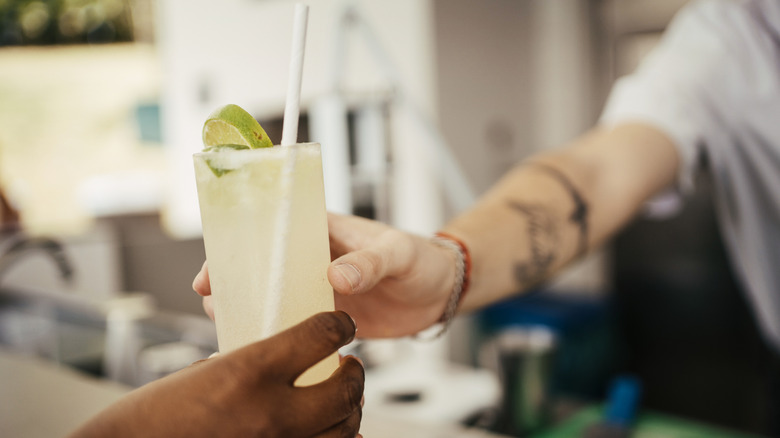 Close-up of a bartender handing a customer a Shady Grove cocktail across a bar