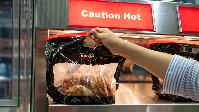 Hand taking rotisserie chicken from case with caution sign above