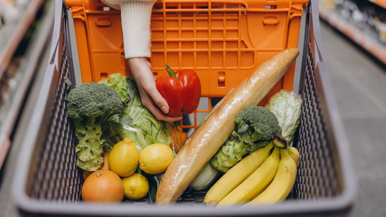 Hand putting a bell pepper in cart on top of a pile of produce