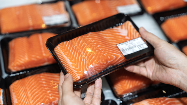 Hands holding sealed pack of salmon at store