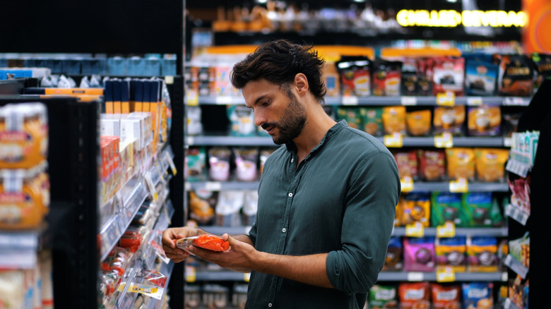 Man looking at package in store among shelved snacks