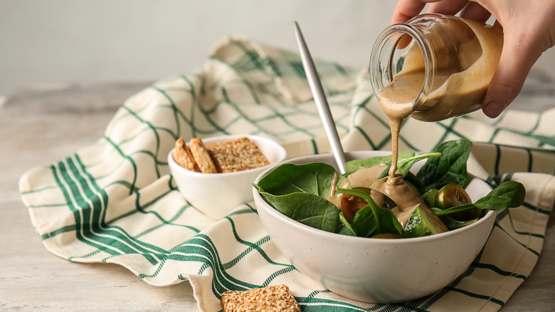 person pouring jarred salad dressing over bowl of greens