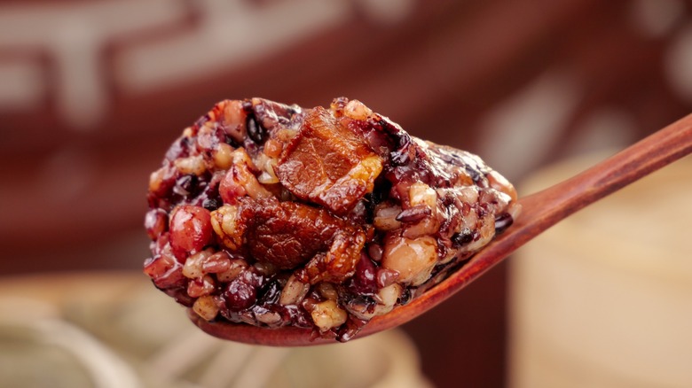 Traditional Chinese eight treasures rice dish with mixed grains, nuts, and dried fruits served on wooden spoon, featuring sticky rice with sweet filling ingredients