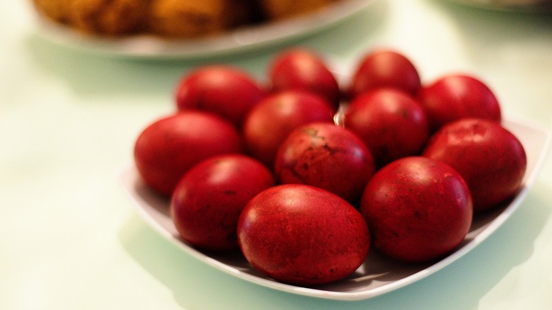 A close-up image of a plate filled with vibrant red dyed eggs, likely part of a Chinese tradition to celebrate a newborn baby's one-month milestone, and other dishes suggesting a celebratory meal.