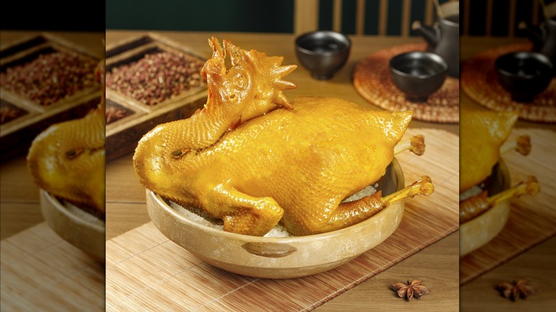 Traditional Hakka salt-baked whole chicken with golden crispy skin served on bamboo steamer with Chinese spices and tea setting