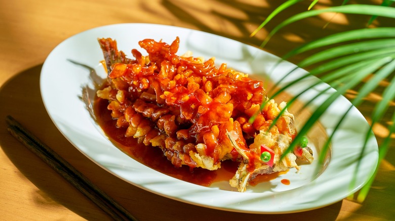 Fried river carp squirrel or songshu yu in sweet and sour sauce with cilantro, sesame seeds and Sichuan pepper in a white bowl. Chinese cuisine