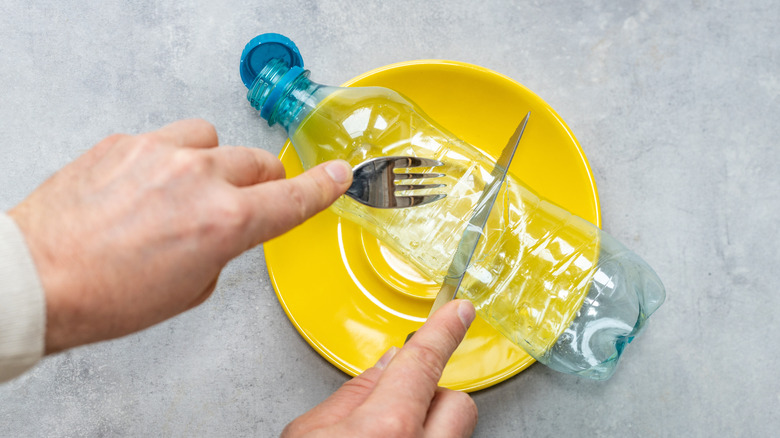 Fork and knife cutting into plastic water bottle on yellow plate