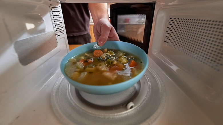 Hand putting a bowl of soup in the microwave