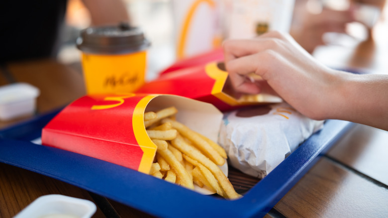 Hand taking some McDonald's French Fries on a blue tray
