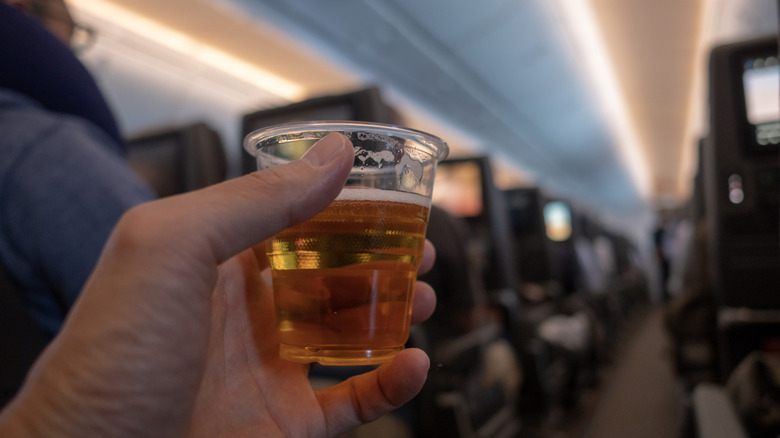 hand holding a cup of beer on an airplane