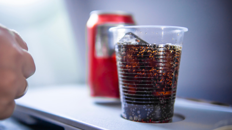 can and cup of soda on airplane tray