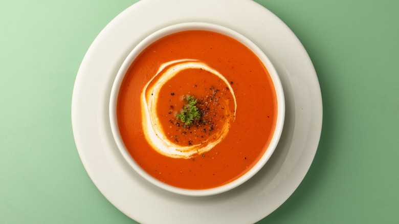 Tomato soup with a swirl of cream in a white bowl on a green background